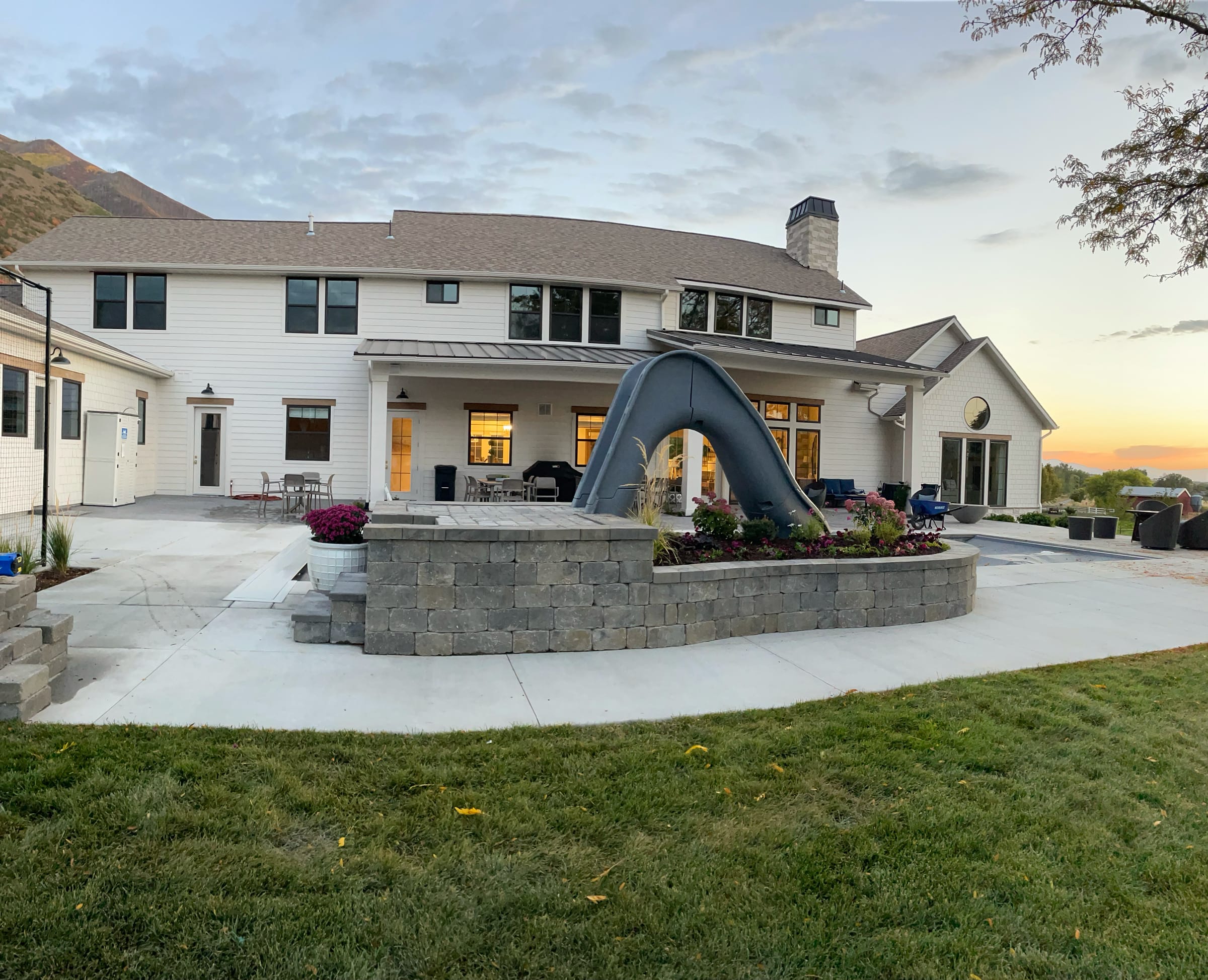 Large white home with a block patio wall, pool slide and lawn at sunset