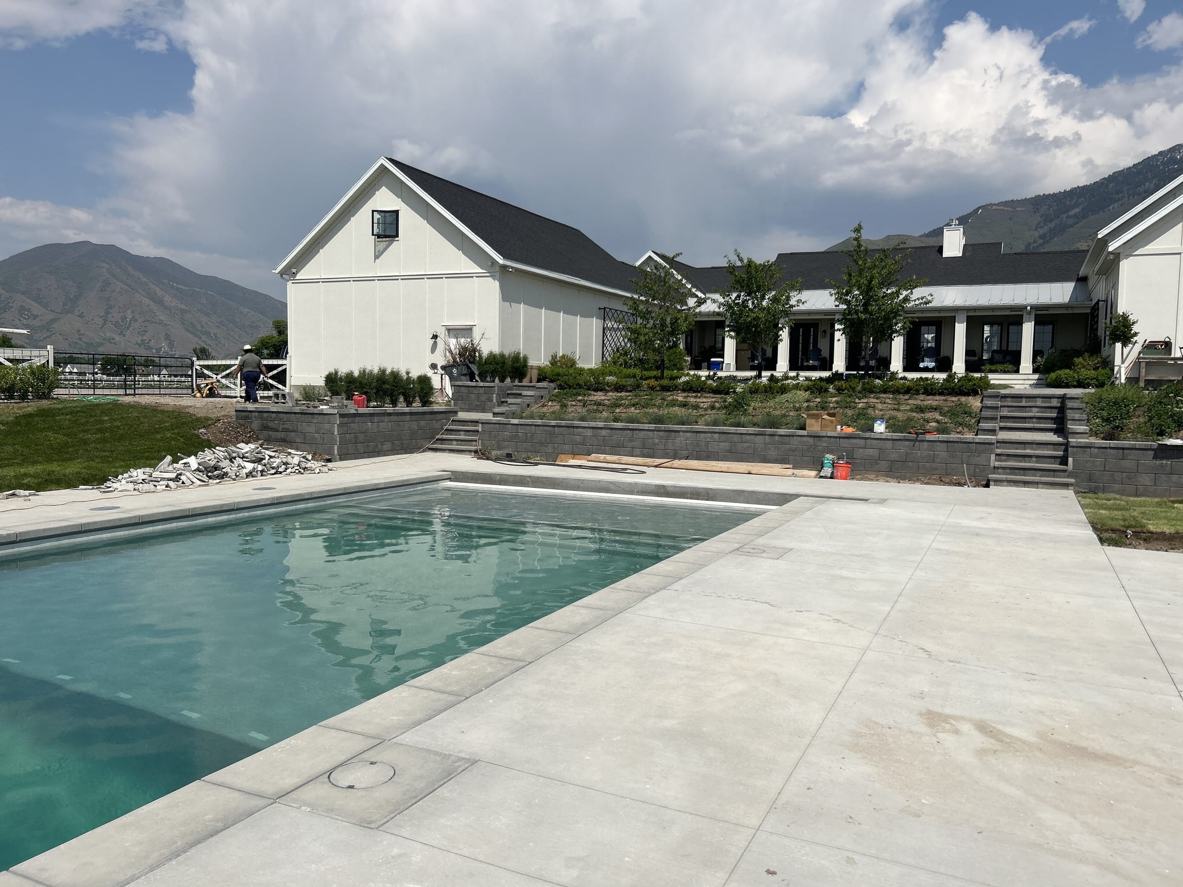 Pool and concrete deck with a white farmhouse and mountains